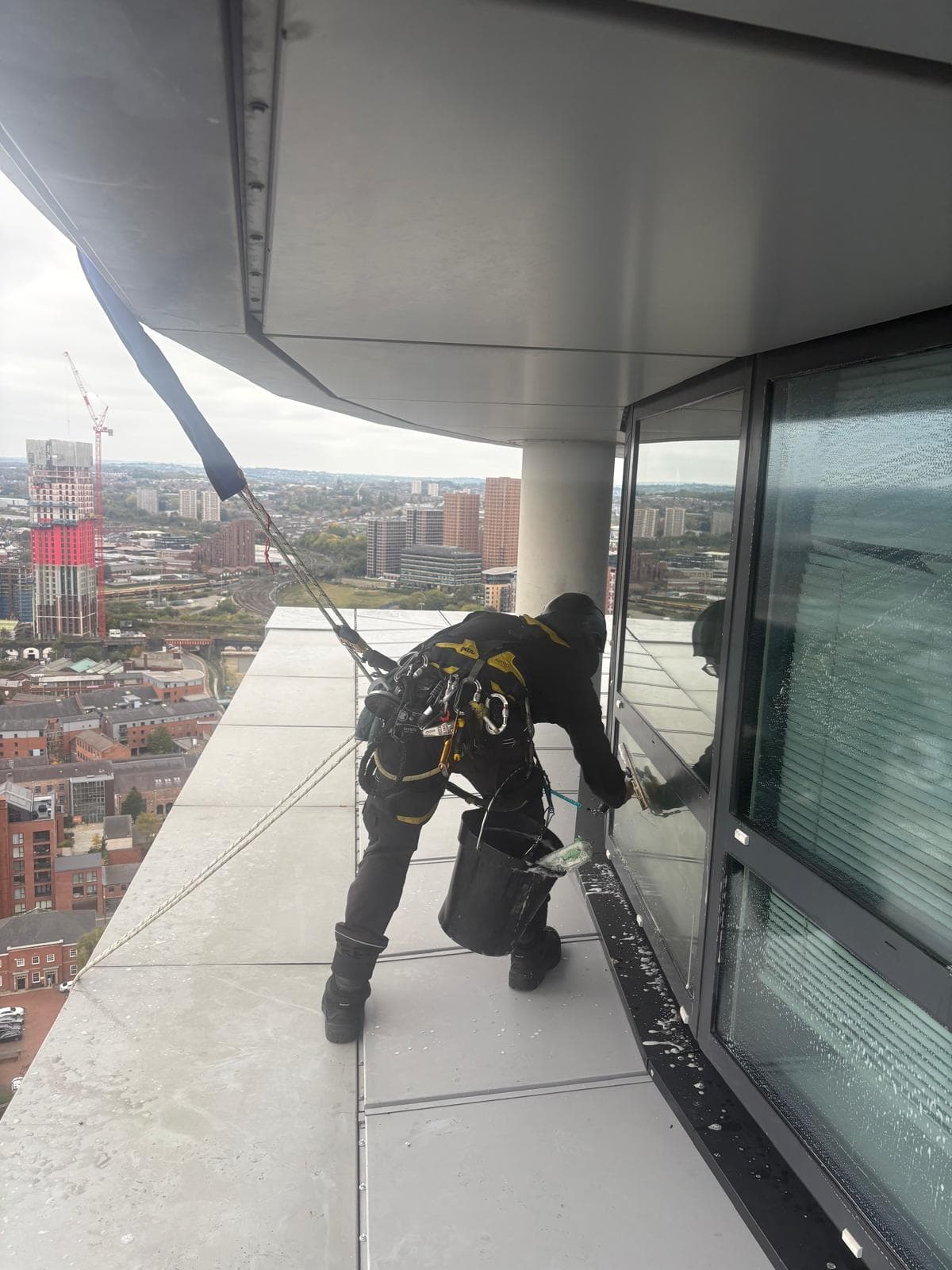 Rope access technician cleaning recessed facade section at Bridgewater Place with Leeds skyline