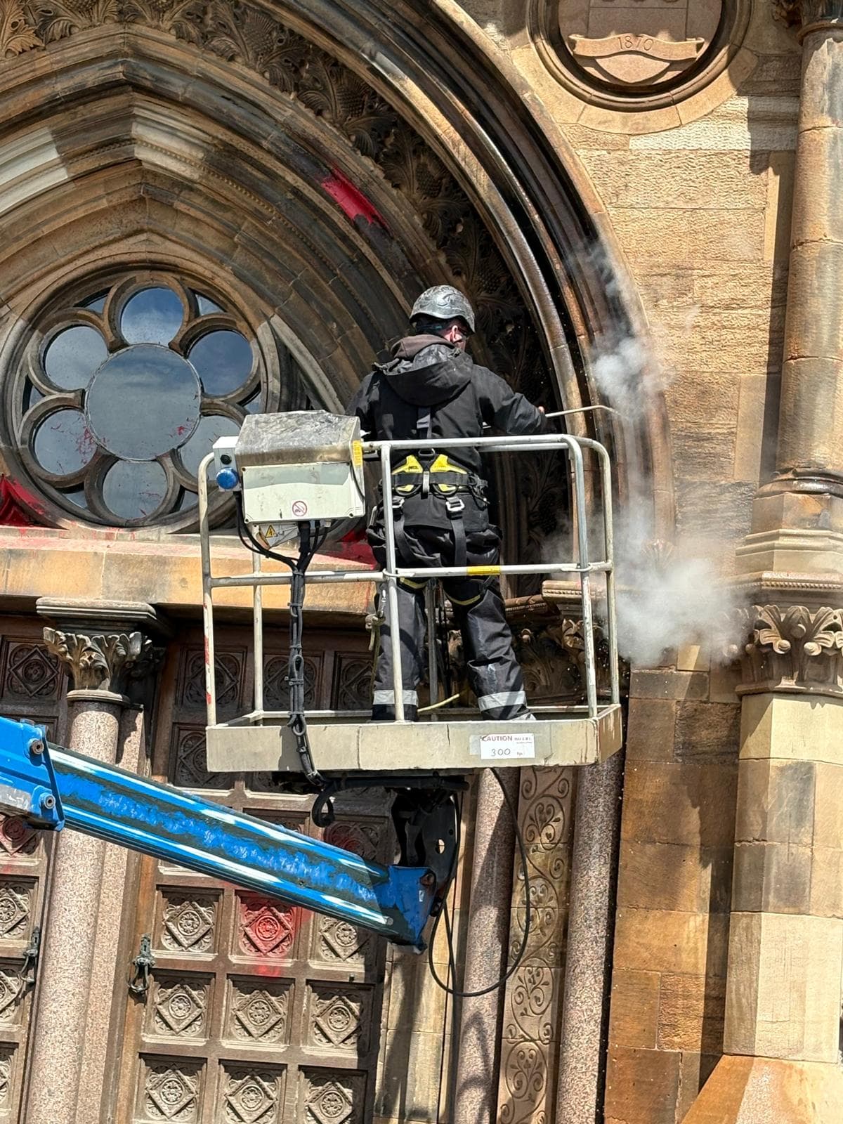DOFF steam cleaning technician on MEWP cleaning heritage Gothic archway at University of Glasgow