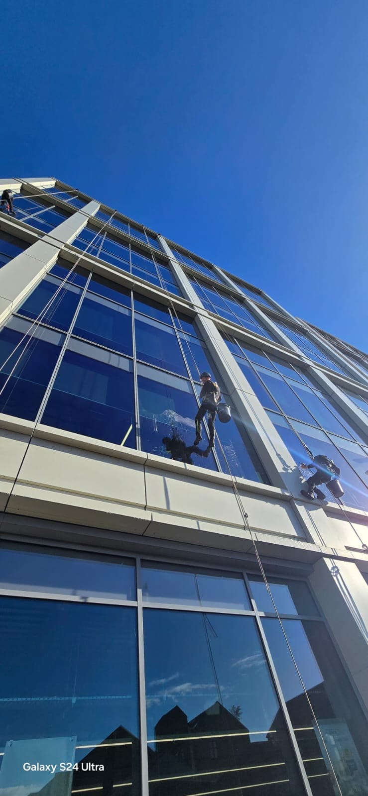 IRATA rope access technicians cleaning windows on modern commercial glass facade